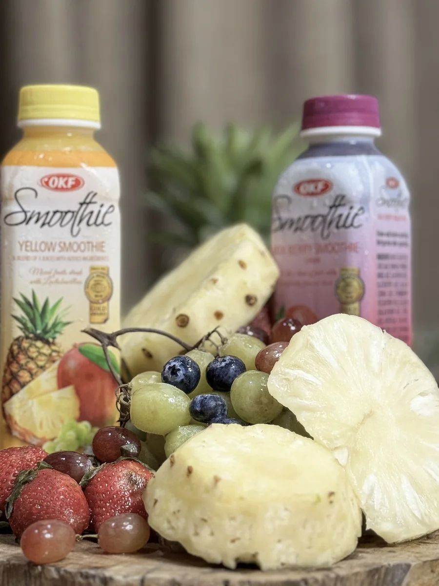 Yellow and Mix Berry OKF smoothies alongside pineapple, grapes and berries